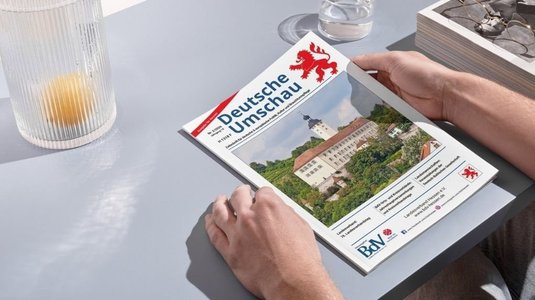 Ausgabe zwei der „Deutschen Umschau“. Bildnachweis: BdV Hessen. Magazin Heft auf einem Tisch mit zwei Händen